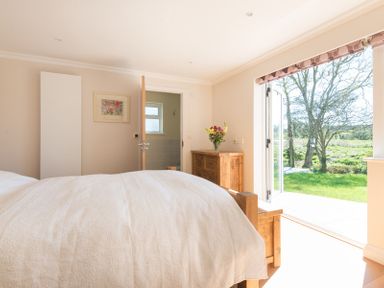A bedroom with a wooden bed and dresser and flowers on the dresser and large open doors to a garden at Chy-An-Dowr in Rock