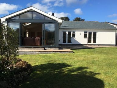 A backyard with a lawn and a white house with large glass doors at Chy-An-Dowr in Rock