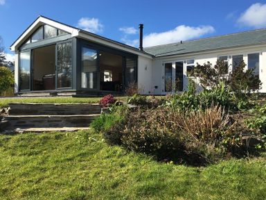 A house with a glass sunroom extension and garden with plants and stone steps at Chy-An-Dowr in Rock