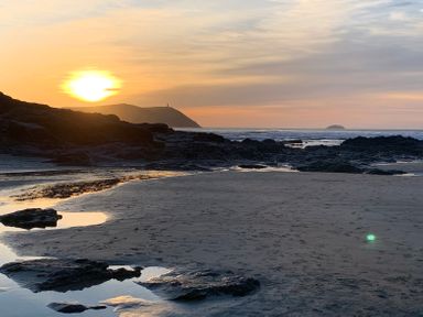 A beach with rock formations and pools of water at sunset with hills and an island in the background at Sandy Lodge Rock in Rock