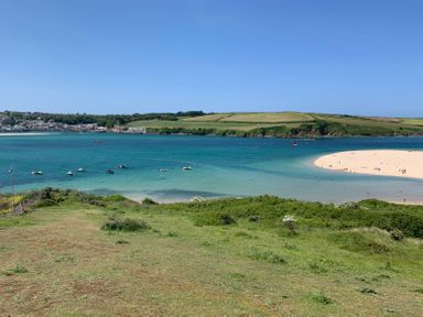 A coastal landscape with green grass foreground a sandy beach and blue water at Sandy Lodge Rock in Rock