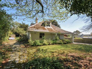 A lawn with a stone pathway leading to a house surrounded by trees and shrubs at Sandy Lodge Rock in Rock