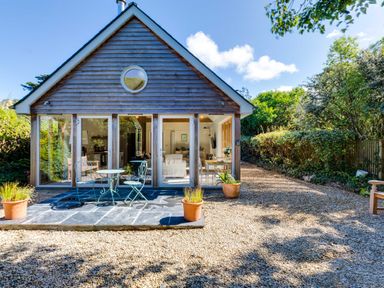 A small wooden house with glass doors and patio furniture outside at Greystones Studio in Daymer Bay