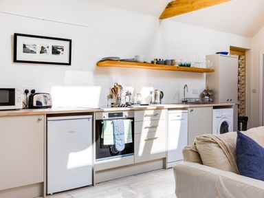 A kitchen with appliances cabinets and a wooden shelf with dishes at Greystones Studio in Daymer Bay