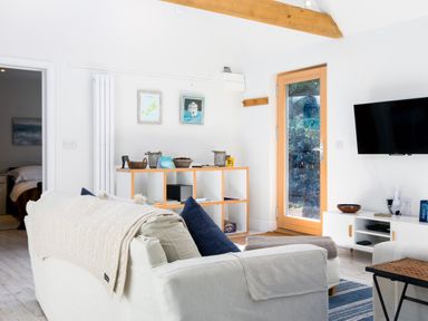 A living room with a white sofa cushions a wooden shelving unit and a wall-mounted television at Greystones Studio in Daymer Bay