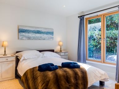 A bedroom with a double bed bedside tables with lamps a window with curtains and a painting above the bed at Greystones Studio in Daymer Bay