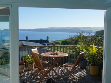 A wooden patio table and chairs with plants on a balcony overlooking the sea at The Porthole in Port Isaac