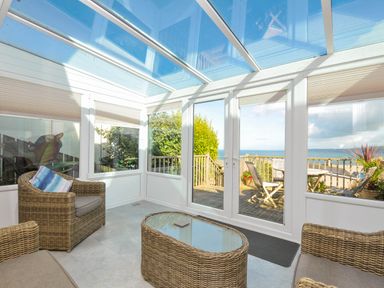 A conservatory with wicker furniture and a view of the sea at The Porthole in Port Isaac