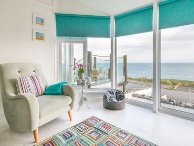 A sitting area with an armchair a small table a bean bag and large windows showing an ocean view at The View in Port Isaac