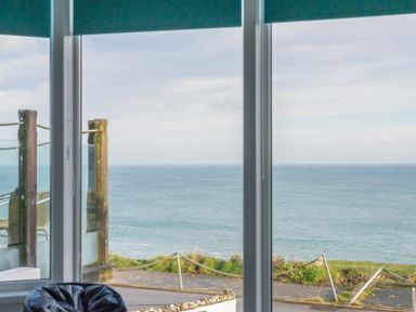 A window with a view of the ocean and a balcony with wooden posts and rope at The View in Port Isaac
