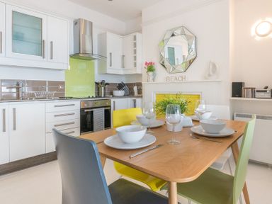 A kitchen with a wooden dining table set with bowls and glasses and multicolored chairs at The View in Port Isaac