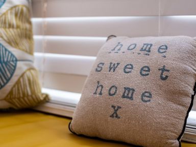 A cushion with home sweet home text on a yellow seat near window blinds