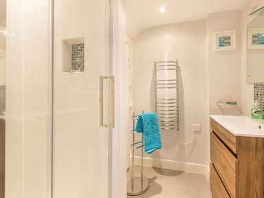 A bathroom with a shower cubicle a metal towel holder with a blue towel a wooden vanity unit and a chrome towel radiator at The View in Port Isaac