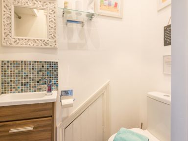 A small bathroom with a toilet, sink with mosaic tile backsplash, mirror, and a towel on the toilet at The View in Port Isaac