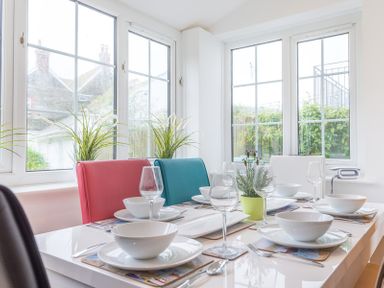 A dining table set with white plates bowls wine glasses and cutlery near windows with plants on the windowsill at Beehive Cottage in Port Isaac