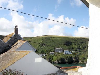 View of rooftops with chimneys a bay with water and green hills in the background at Beehive Cottage in Port Isaac