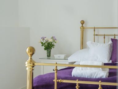 A bedroom with a brass bed frame a white pillow purple bedding white towels on the bed and a bedside table with a vase of flowers at Beehive Cottage in Port Isaac