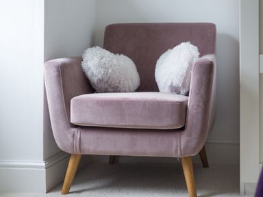 A pink armchair with two white fluffy pillows in a corner at Beehive Cottage in Port Isaac