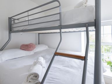A bedroom with a metal bunk bed with towels and a heart shaped pillow on a lower bed at Beehive Cottage in Port Isaac