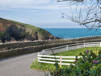 A coastal road with a stone wall and white fence overlooking the sea and a grassy hill at Beehive Cottage in Port Isaac