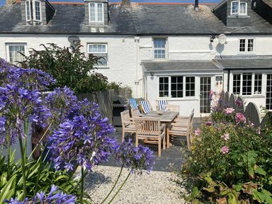 A garden patio with a wooden table and chairs surrounded by purple flowers at Beehive Cottage in Port Isaac