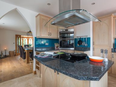 A kitchen with granite countertops and a stove next to a dining area with a wooden table and dark chairs at Fairholme in Port Isaac