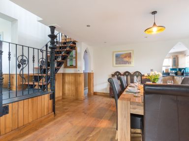 A dining area with a wooden table and leather chairs next to a black metal staircase at Fairholme in Port Isaac