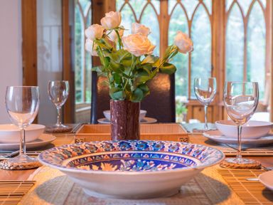 A dining table with a large colorful bowl white roses in a vase wine glasses and white plates at Fairholme in Port Isaac