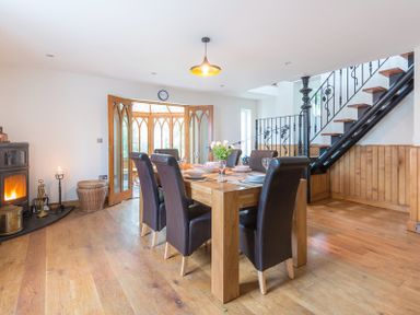A dining room with a wooden table and six leather chairs near a wood stove and staircase at Fairholme in Port Isaac