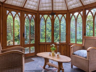 A sunroom with wicker chairs and a wooden table with flowers and cups at Fairholme in Port Isaac
