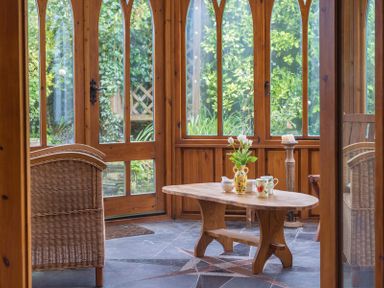 A sunroom with wooden framed windows and door a wooden coffee table with flowers and mugs and wicker chairs at Fairholme in Port Isaac