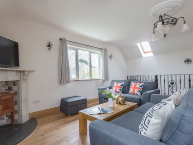 A living room with two sofas with Union Jack cushions a wooden coffee table flowers and a brass helmet on the table a TV mounted above a fireplace a window with curtains and a skylight at Fairholme in Port Isaac