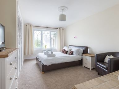 A bedroom with a bed with white bedding next to a bedside table and a brown armchair at Fairholme in Port Isaac