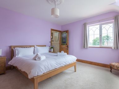 A bedroom with a wooden bed and white bedding near a window with curtains and a wooden door at Fairholme in Port Isaac