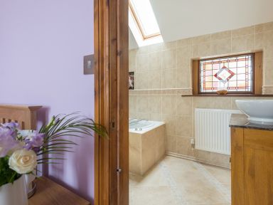 A bathroom with a tiled bathtub and stained glass window next to a bedroom with flowers on a table at Fairholme in Port Isaac