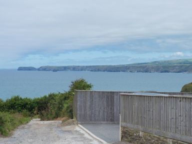 A coastal view with cliffs and ocean seen from a gravel path and wooden fence at Fairholme in Port Isaac