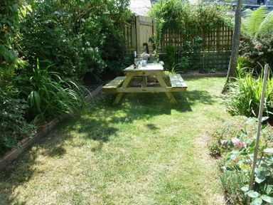 A garden area with a wooden picnic table on grass surrounded by plants and a wooden fence at Fairholme in Port Isaac