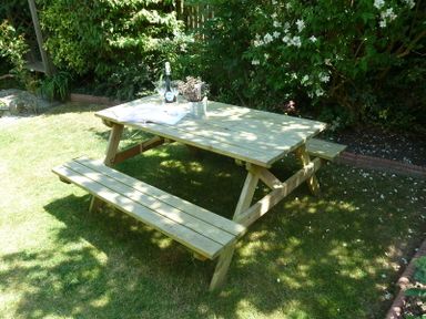 A wooden picnic table with benches in a garden with plants and flowers at Fairholme in Port Isaac
