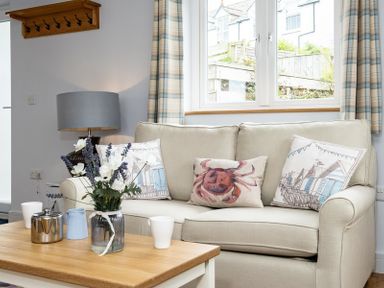 A living room with a beige sofa with cushions a wooden coffee table with a flower vase and a lamp on a side table at The Hideaway in Port Isaac