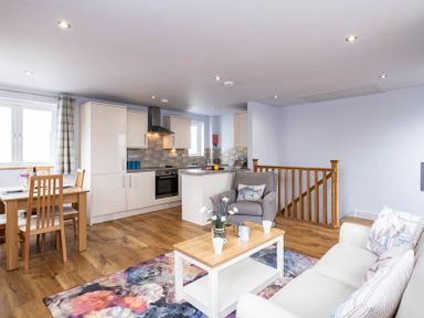 An open plan living area with a kitchen dining table sofa armchair coffee table and floral rug at The Hideaway in Port Isaac