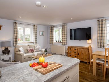 A living room with a sofa and cushions a wooden cabinet under a wall-mounted television and a table with chairs at The Hideaway in Port Isaac
