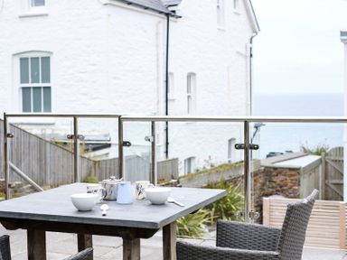 An outdoor seating area with a table set for tea on a patio near white buildings at The Hideaway in Port Isaac