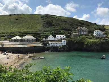 A coastal village with houses on a hillside near a small beach and turquoise water at The Hideaway in Port Isaac