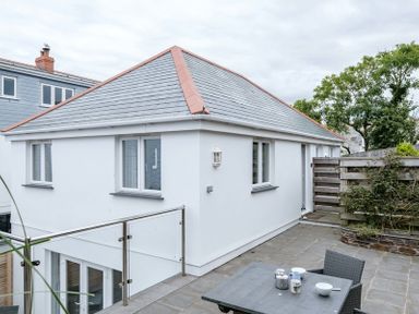 An outdoor patio area with a table and chairs next to a white two-story building with windows and a gray tiled roof at The Hideaway in Port Isaac
