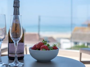 A table with a bottle of sparkling wine two empty glasses and a bowl of strawberries with a beach view at Point Break in Polzeath