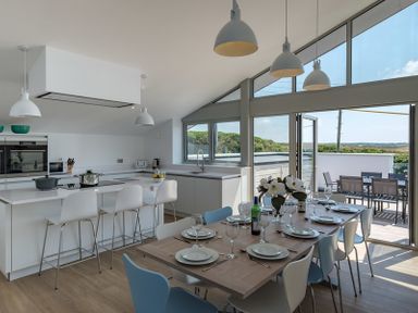 A kitchen with a dining table set with plates and glasses and an outdoor seating area at Point Break in Polzeath