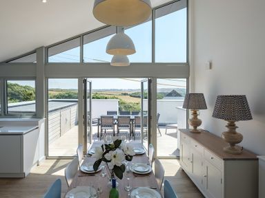 A dining area with a wooden table set for six and two patterned lamps on a sideboard at Point Break in Polzeath