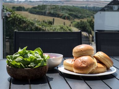 A table with a bowl of lettuce a bowl of cherry tomatoes and a plate of bread rolls outside at Point Break in Polzeath