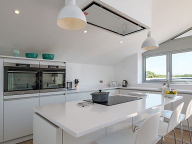 A kitchen with a white island and three chairs with windows and built in ovens at Point Break in Polzeath