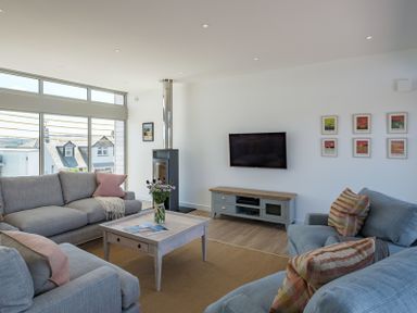 A living room with gray sofas a wooden coffee table a wall mounted TV and a stove at Point Break in Polzeath